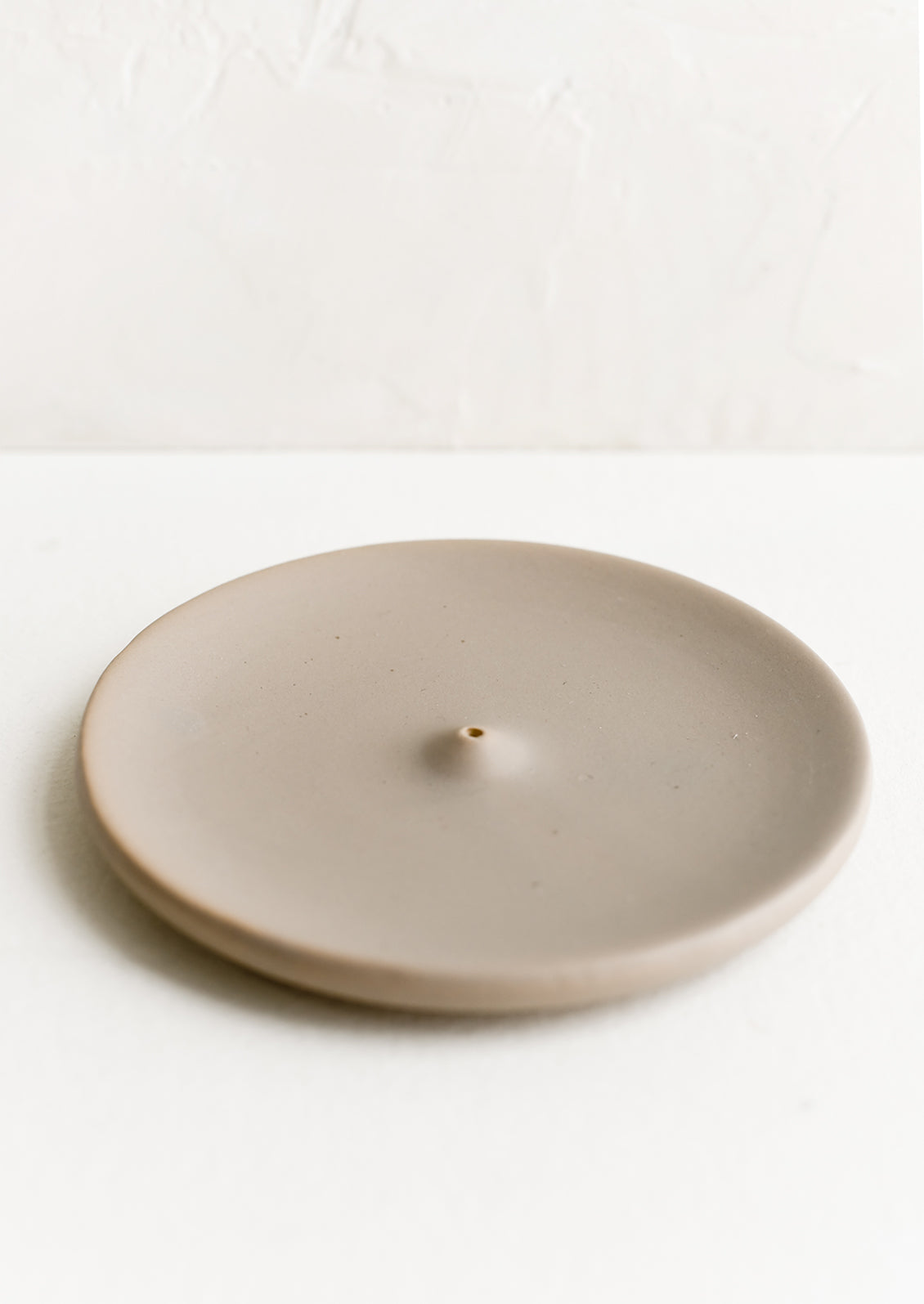 A round ceramic incense holder in matte taupe