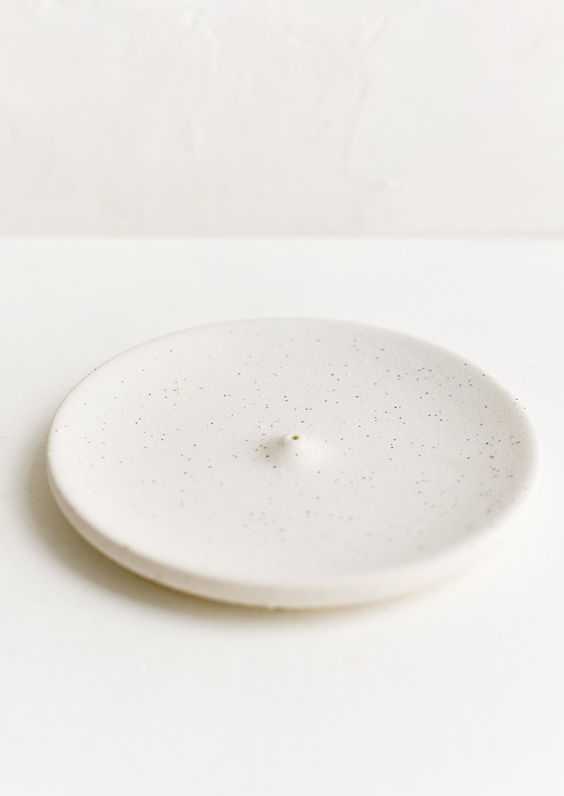 A round ceramic incense holder in matte speckled white.