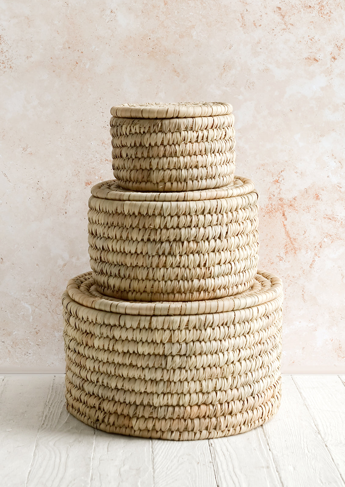 Three round, palm leaf storage baskets with lids in incremental sizes.