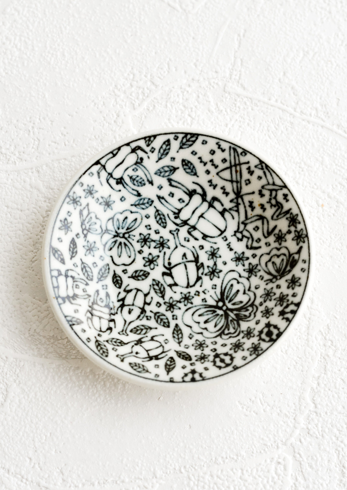 A round ceramic trinket dish in black and white with insect print.