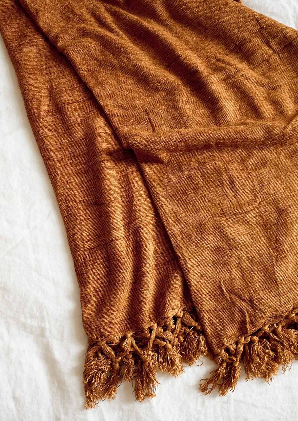 A chenille throw with knotted tassel trim in nutmeg copper color.