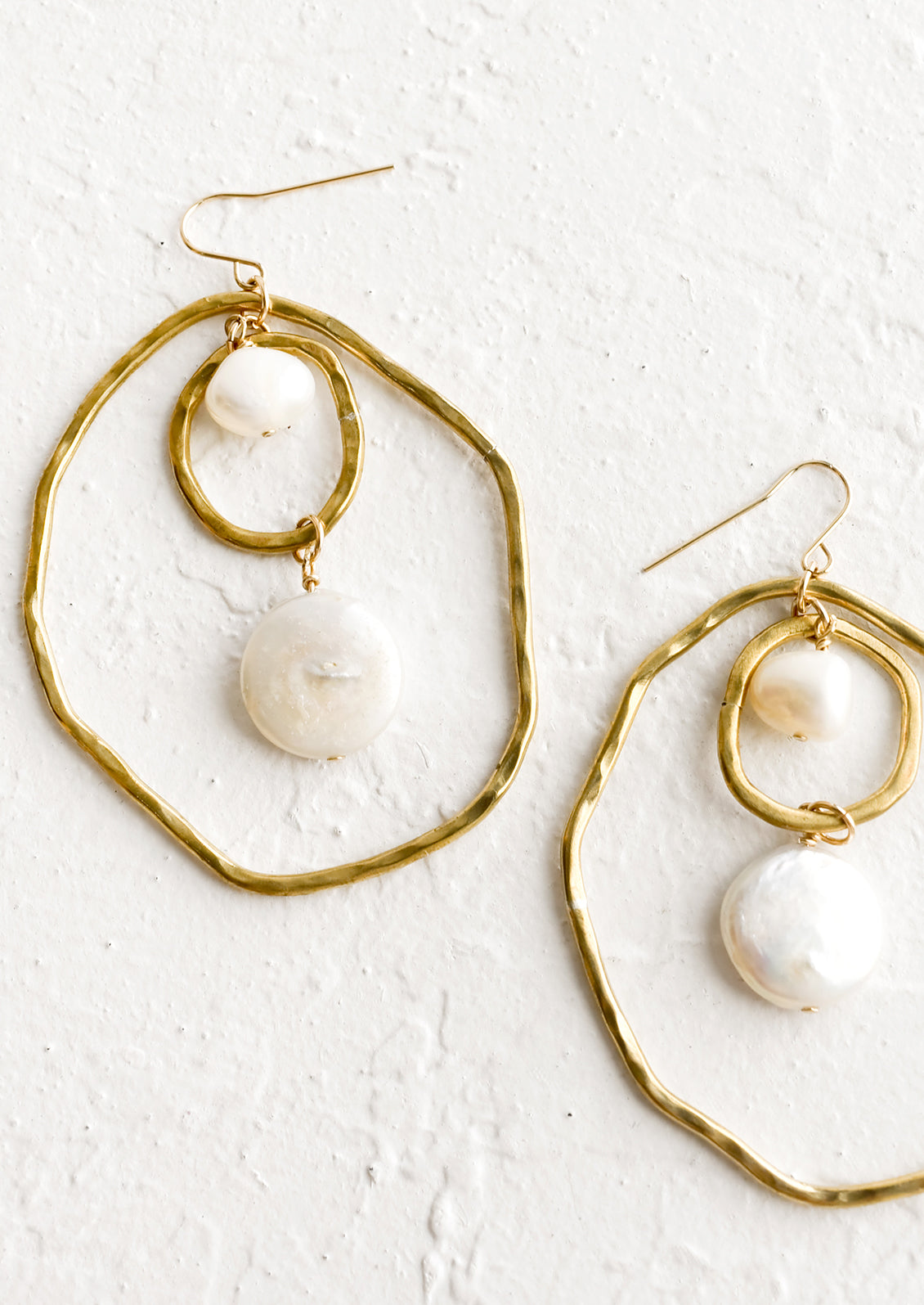 A pair of gold earrings with freeform hoops and floating pearls.