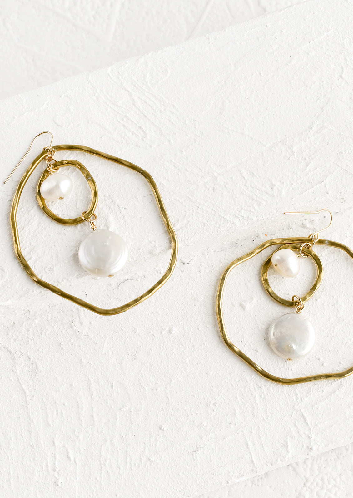 A pair of gold earrings with freeform hoops and floating pearls.