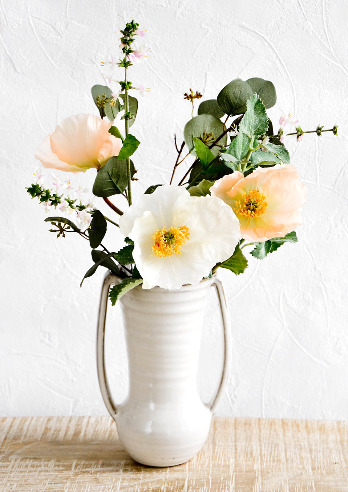 Glossy ceramic vase with side handles, housing floral bouquet with poppies and wild basil flowers