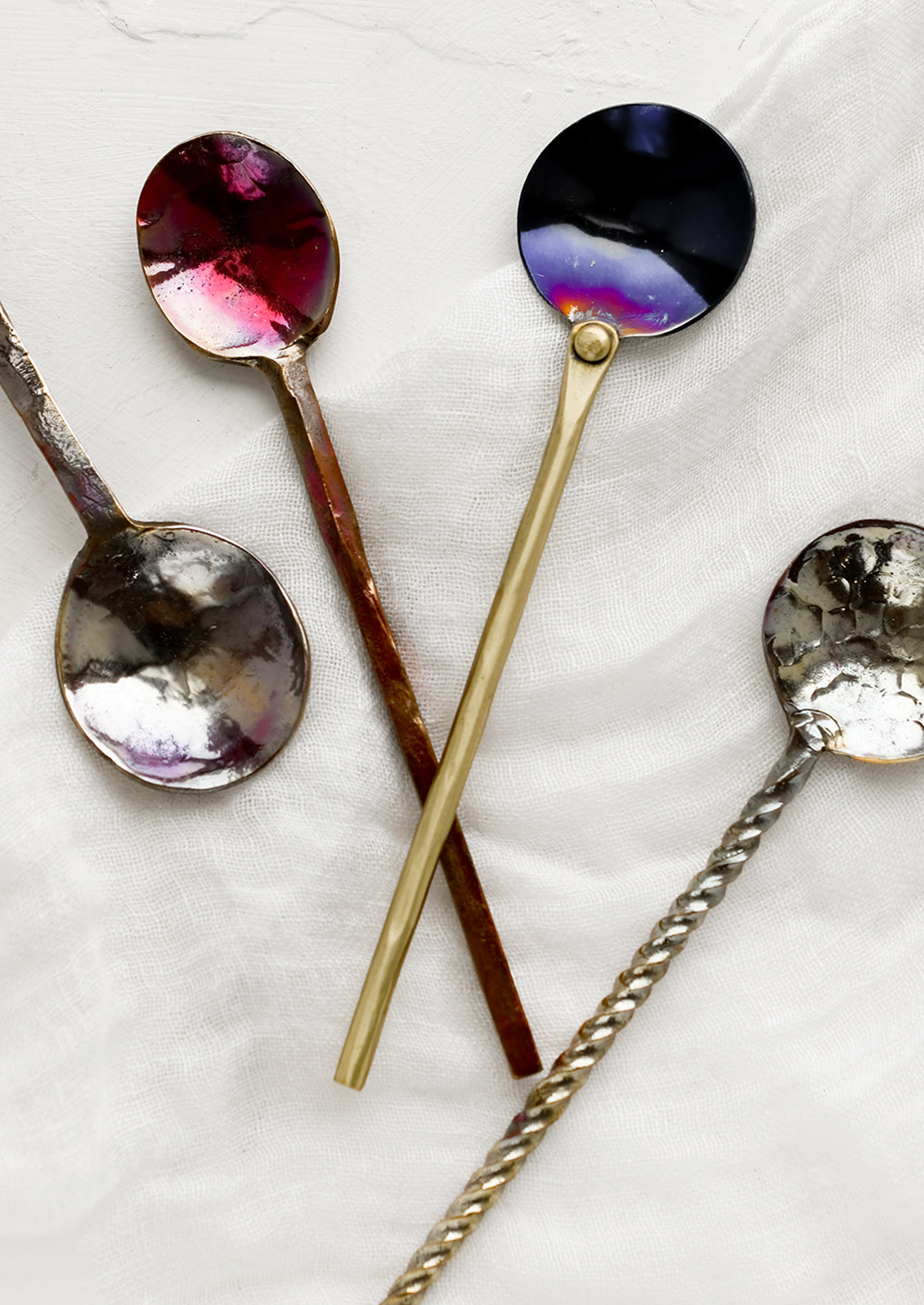 A variety of oxidized metal spoons in different finishes and handle types.