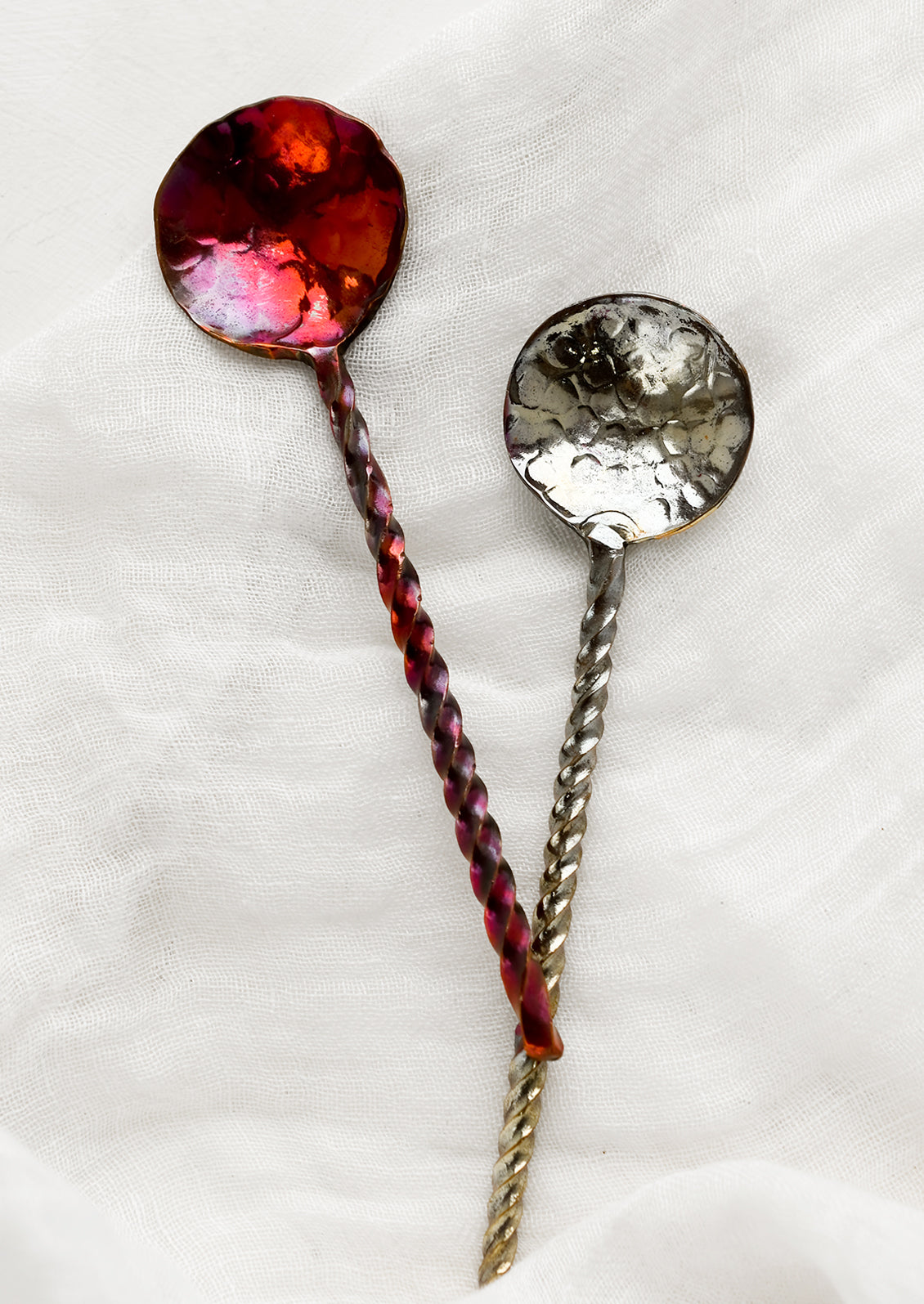 Oxidized metal spoons with twisted handles and oil slick finishes.