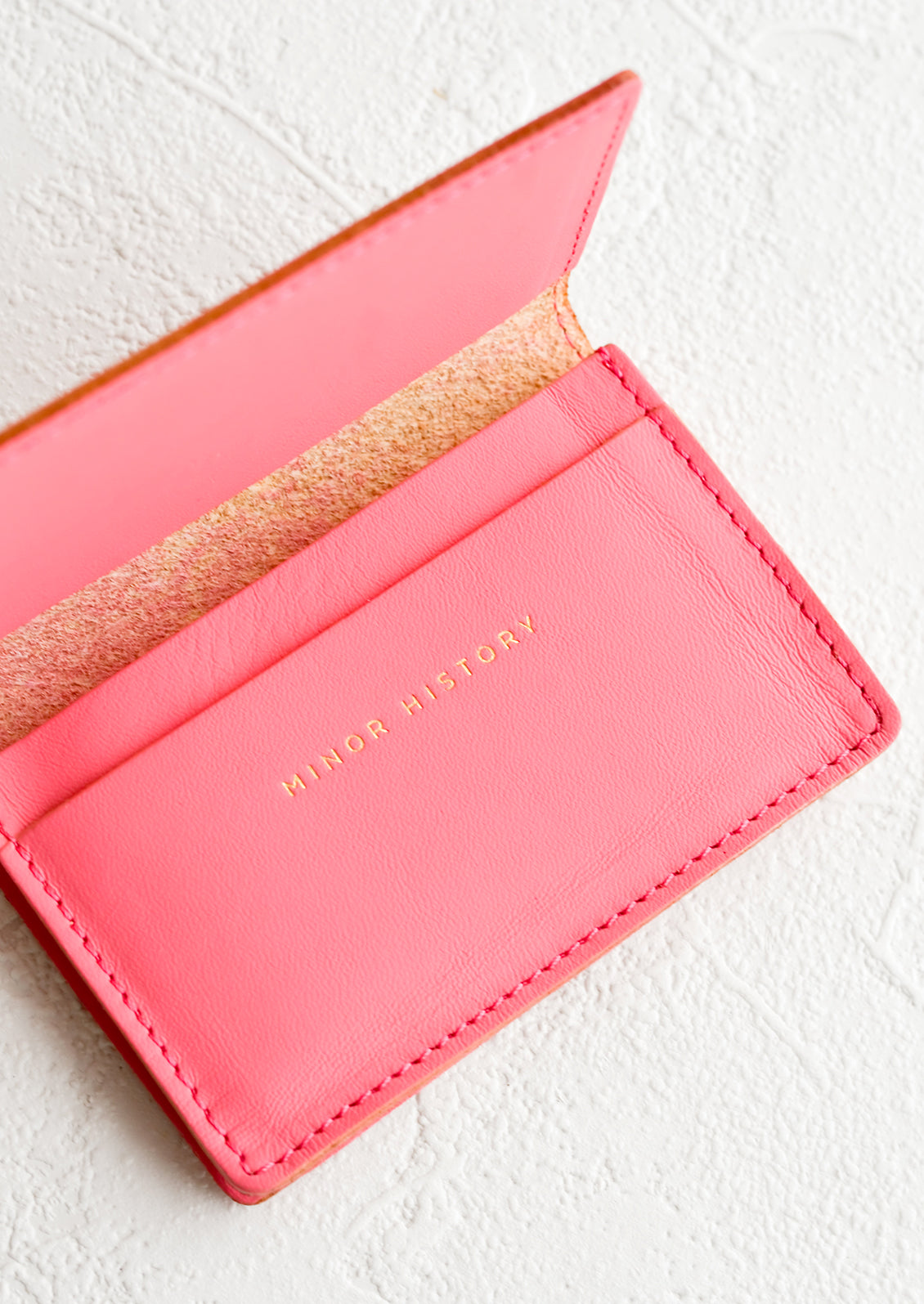 A bright pink leather card holder wallet with interior sleeve and gold branding.