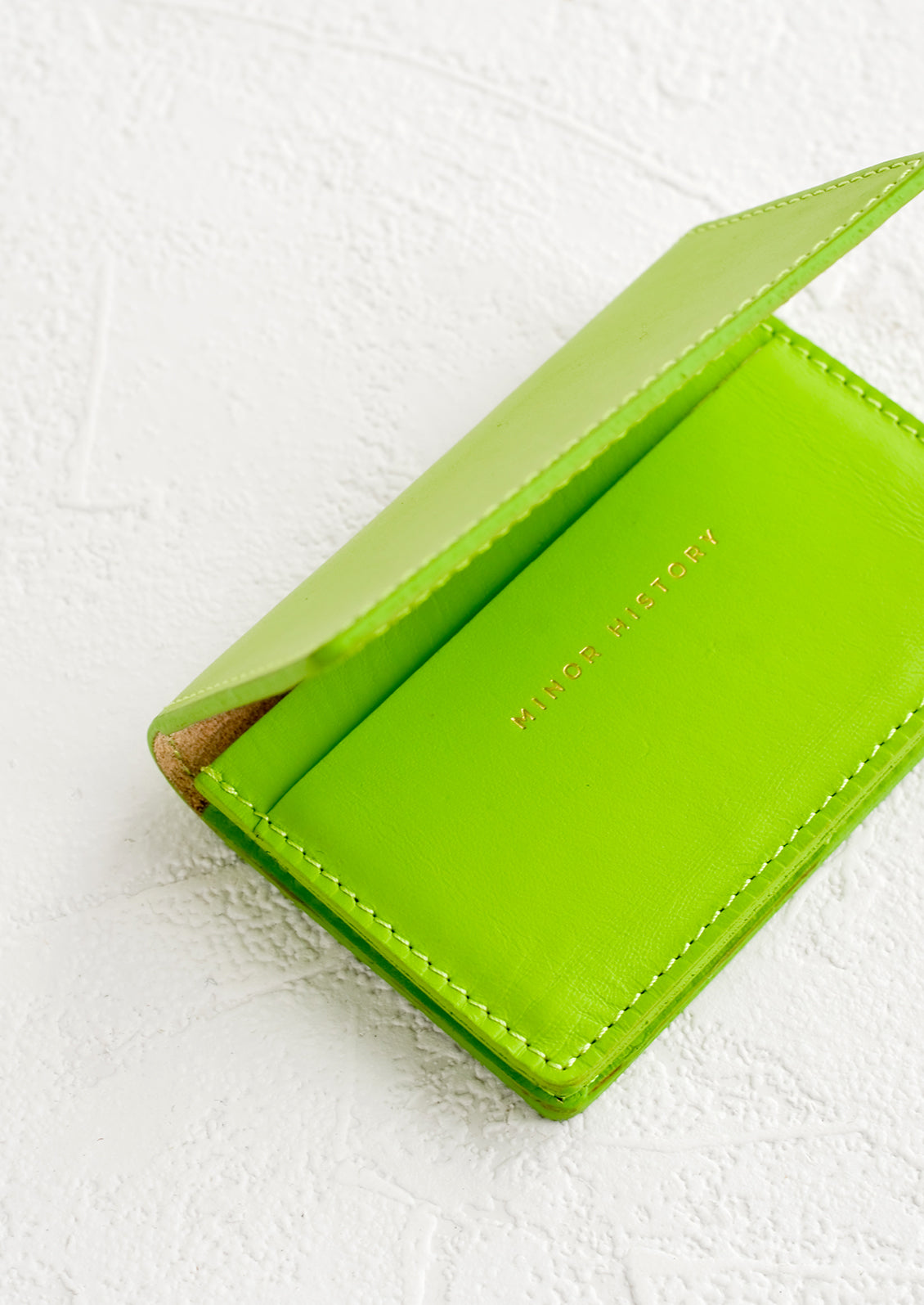 A lime green leather card holder wallet with interior sleeve and gold branding.