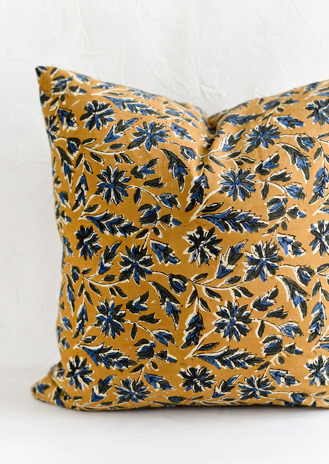 A block printed pillow with floral motif in blue and black on tan.