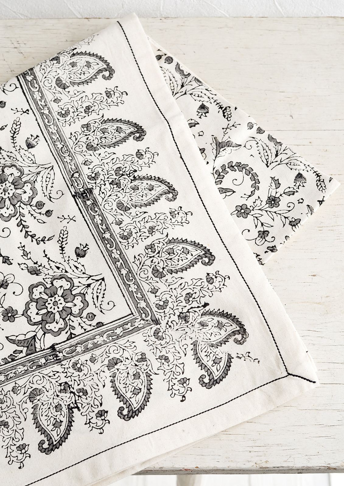 A block printed cotton tablecloth with black stitching and grey floral paisley pattern.