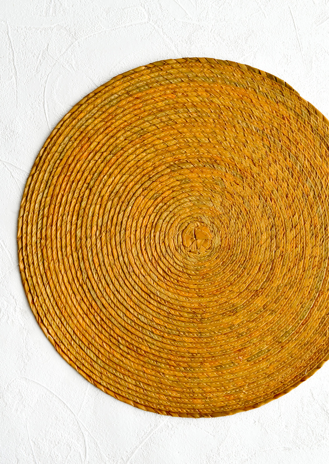 A round woven straw placemat in ochre color.