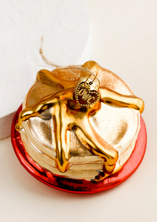 A holiday ornament of a stack of pancakes on a red plate.