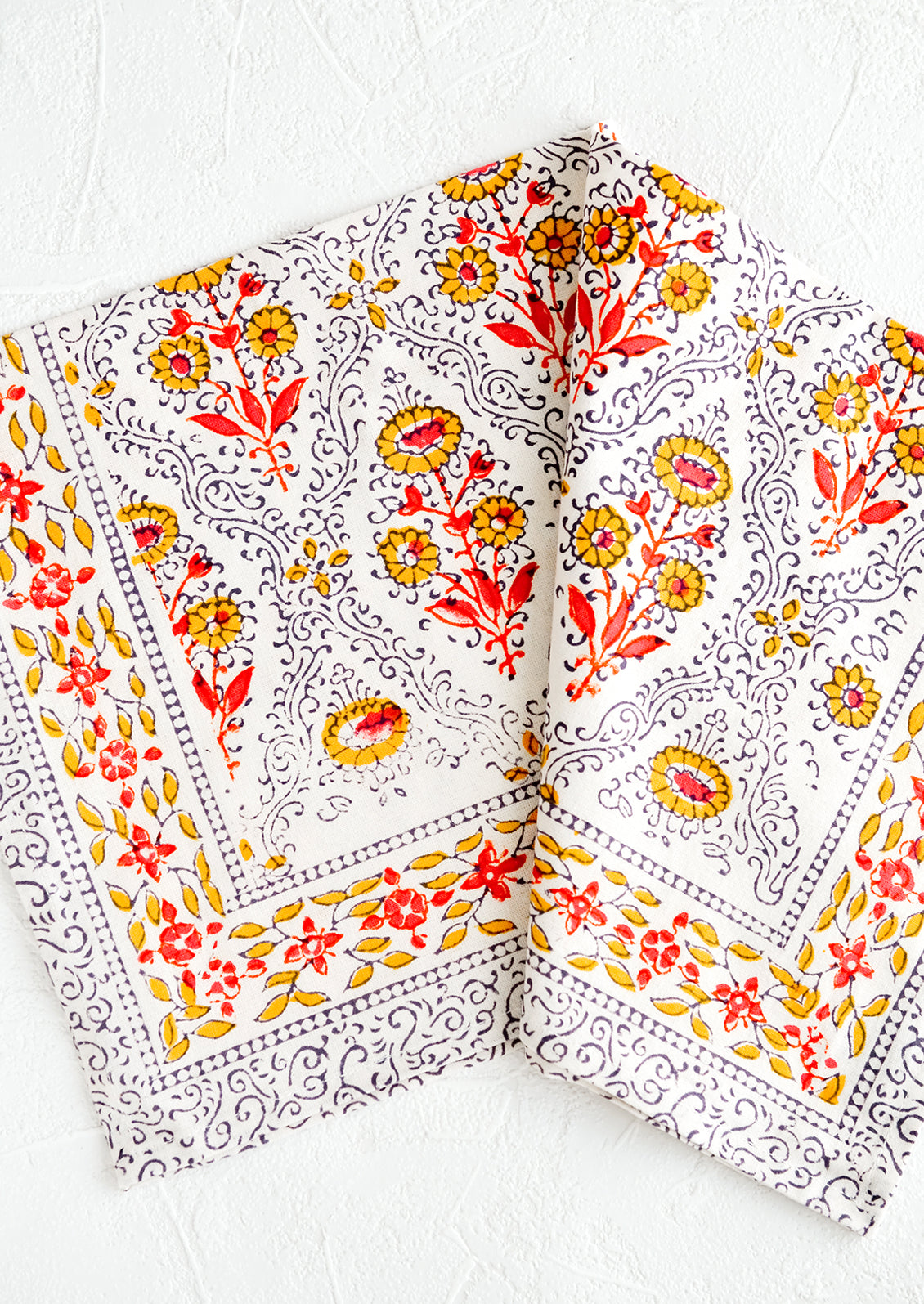 A block printed napkin in yellow, red, black and white floral pattern.