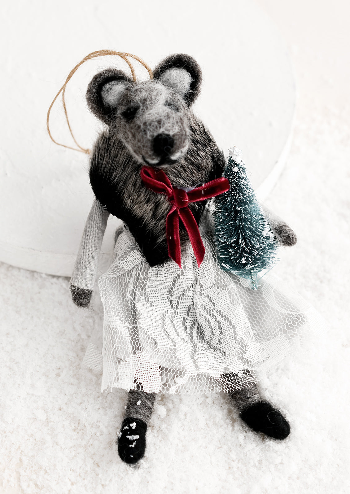 A felted holiday ornament of a badger wearing a dress, holding a tiny christmas tree.