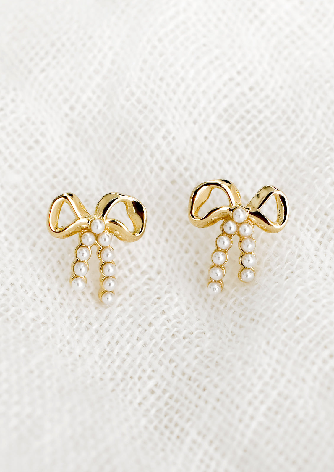 A pair of gold bow studs with tiny pearl detailing on "strings".