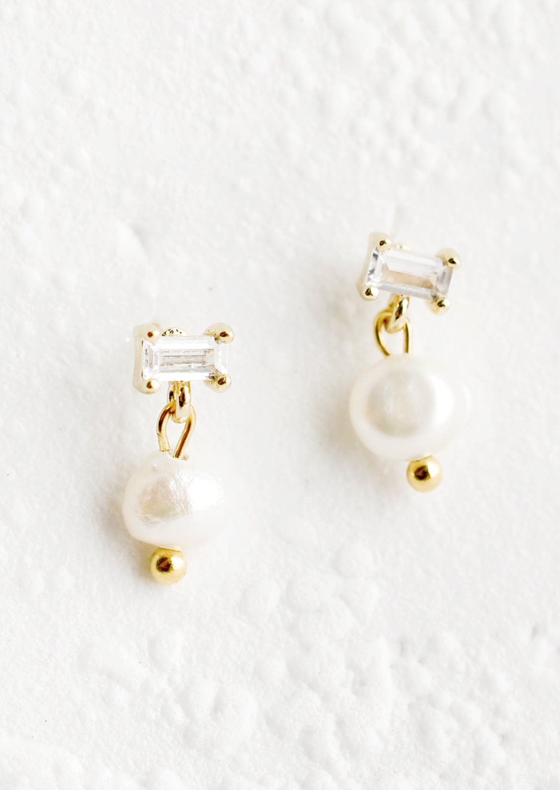 A pair of post back earrings with clear baguette crystal post and a dangling freshwater pearl.