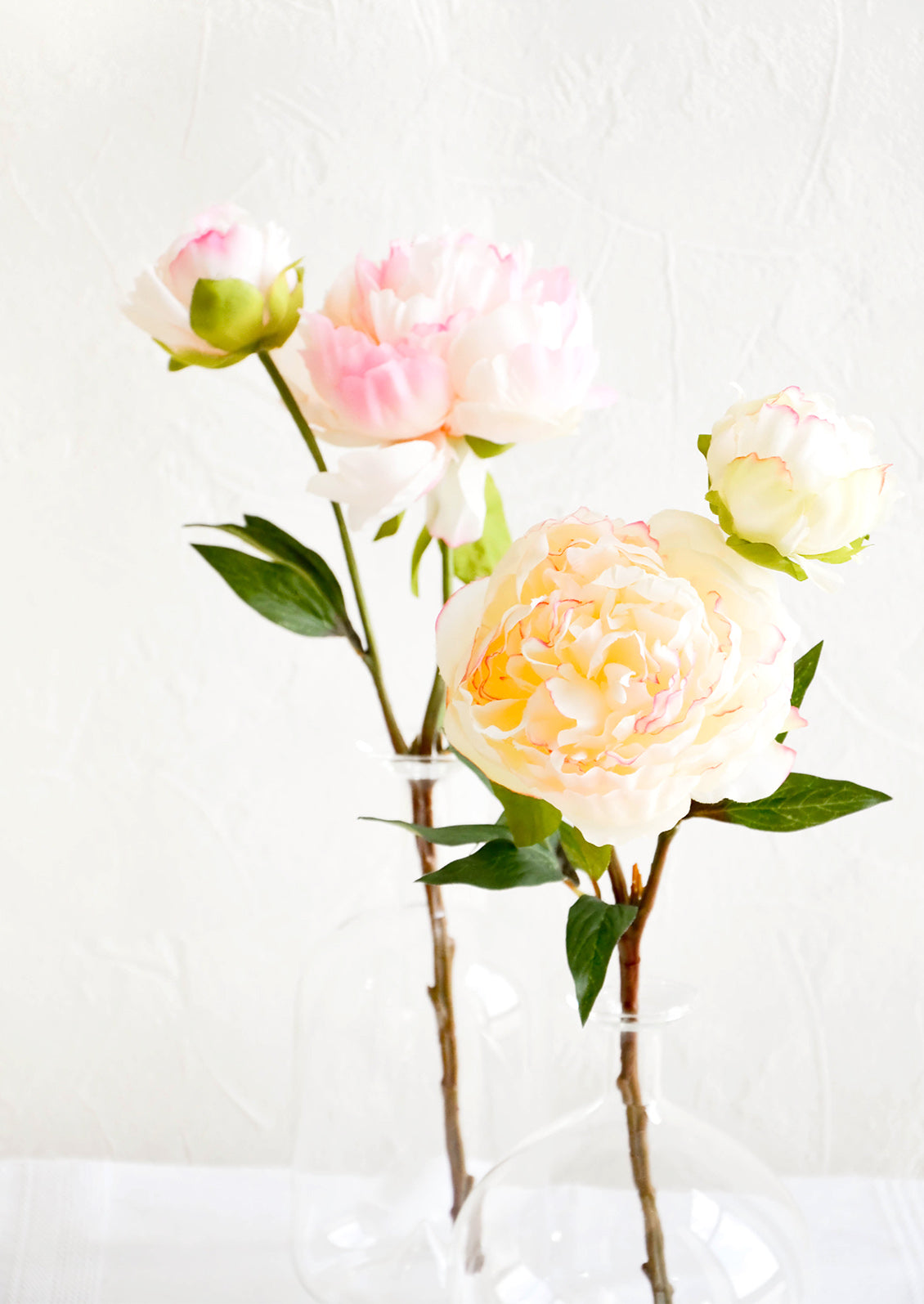 Realistic faux peony flowers in white and pink, displayed in glass vases