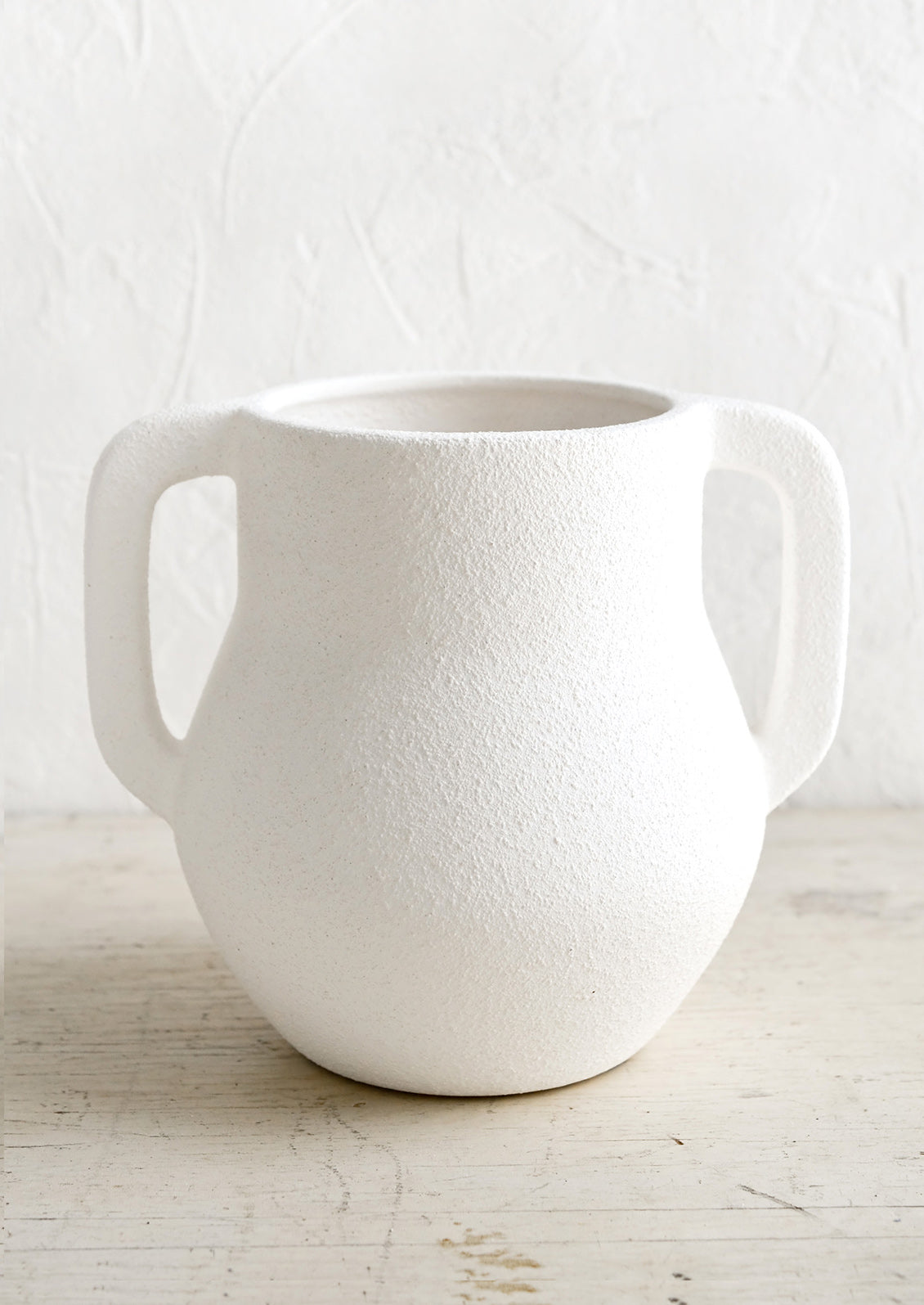 A textured matte vase in white ceramic with handles at sides.