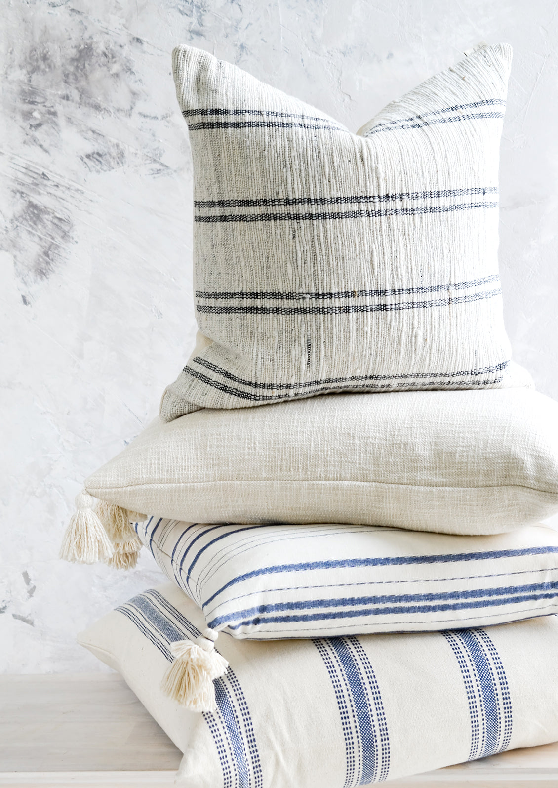 A stack of pillows in white, blue and cream colors.