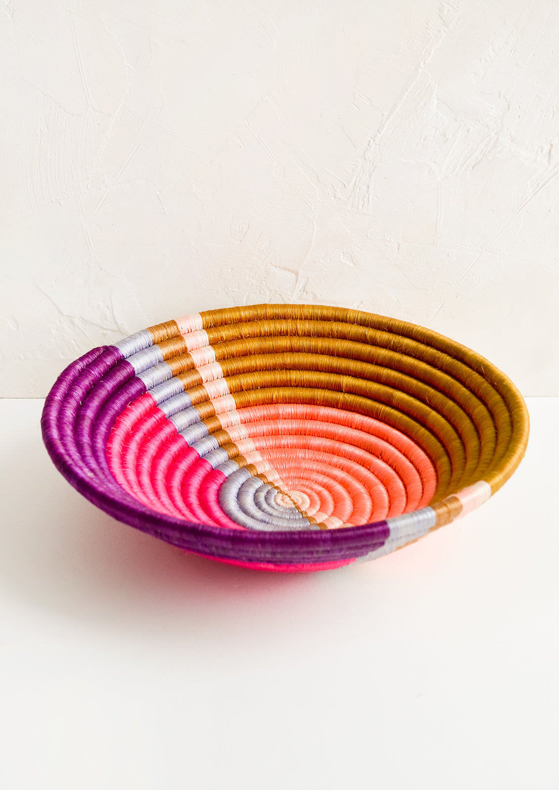 A round colorful woven sweetgrass basket with multicolor sunset design.