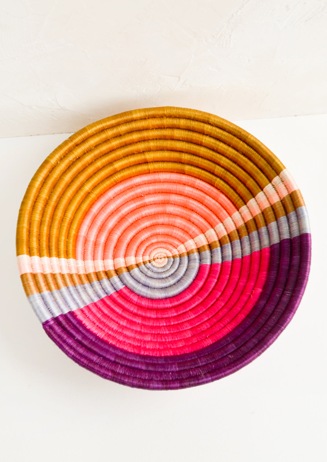 A round colorful woven sweetgrass basket with multicolor sunset design.