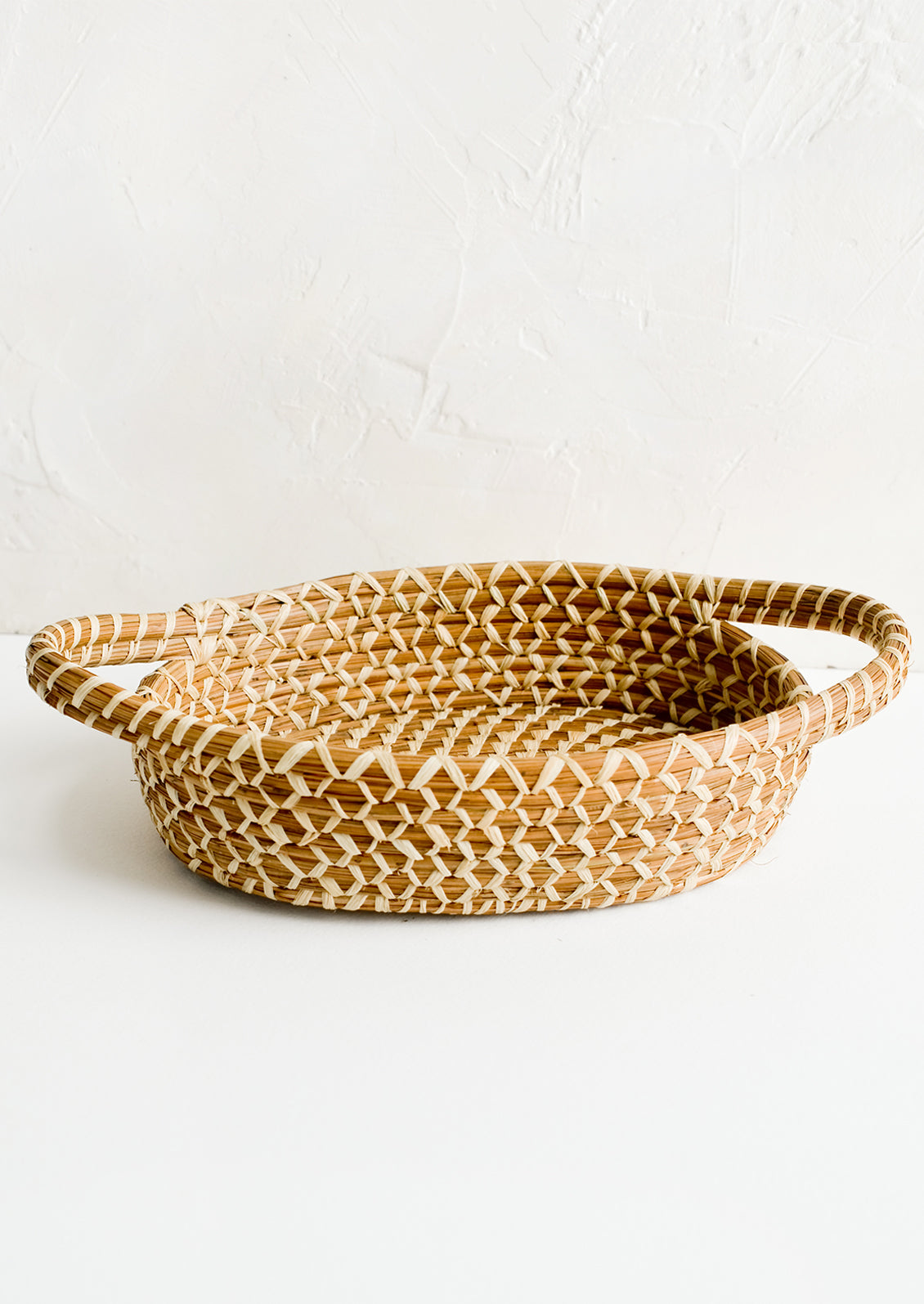 A shallow, oval shaped basket with handles at sides.