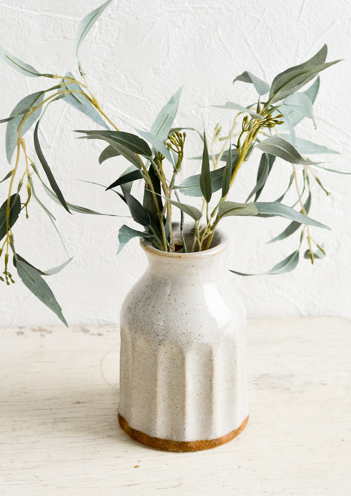 A glossy ceramic vase in natural speckled color, with eucalyptus leaves.