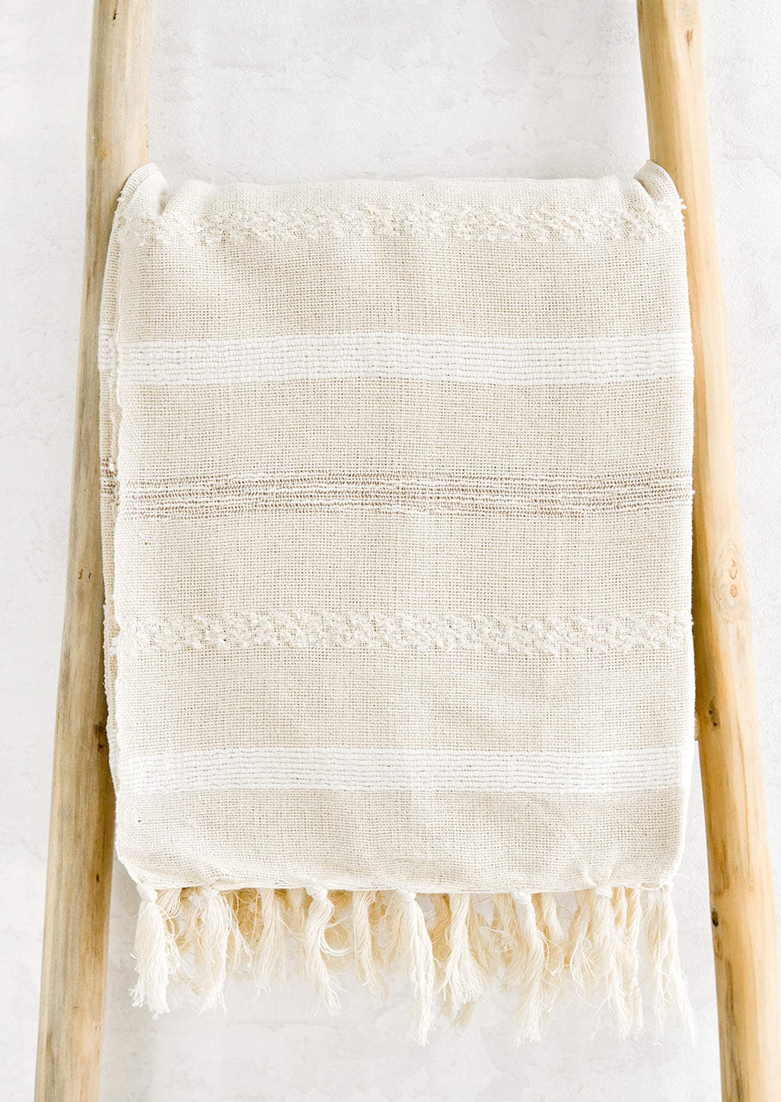 A woven cotton gauze blanket with textured stripes in white on a display ladder.