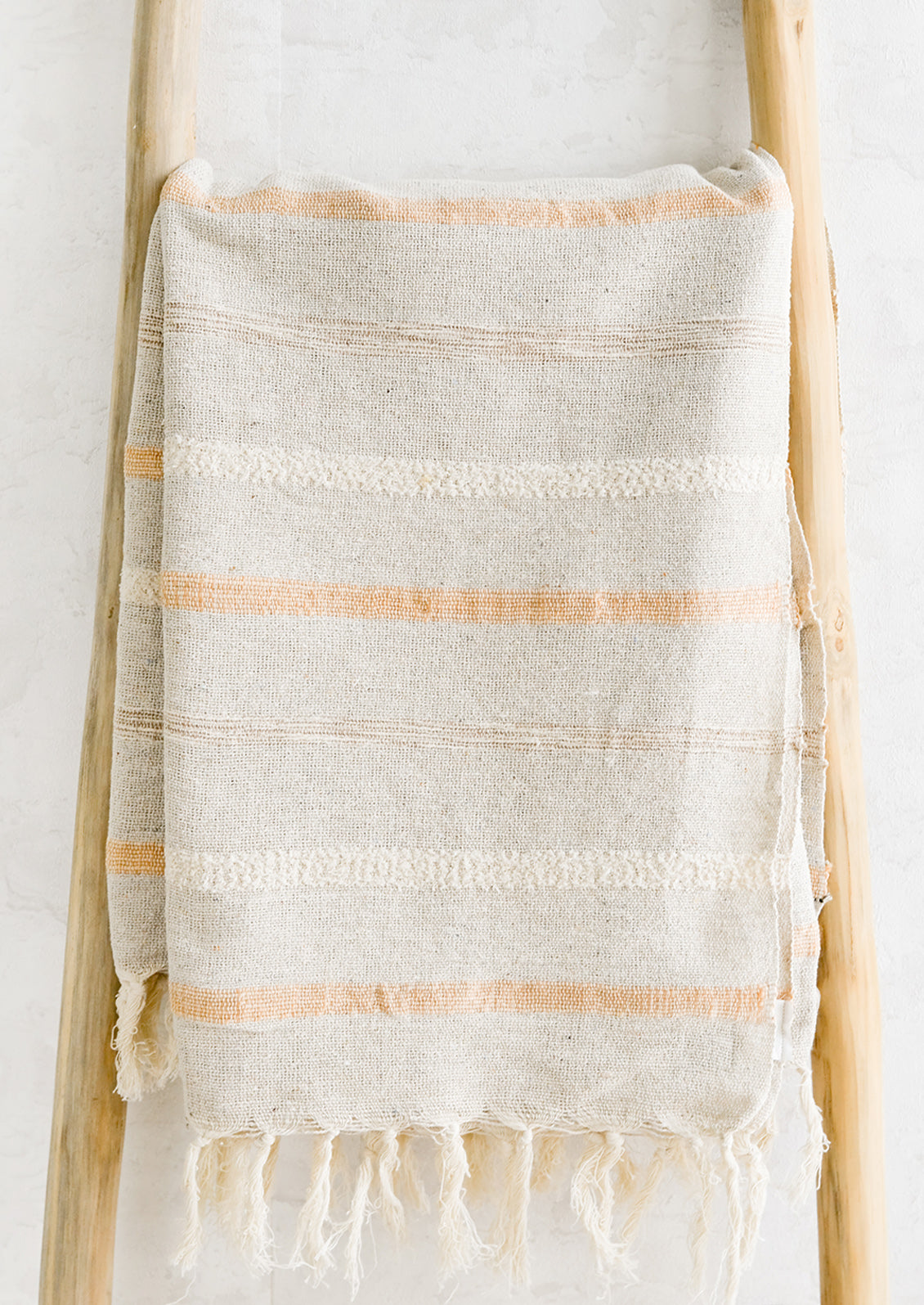 A woven cotton gauze blanket with textured stripes in apricot on a display ladder.