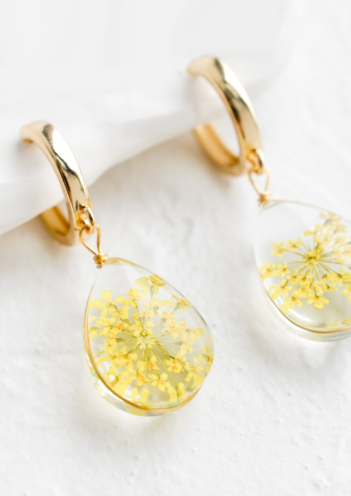 A pair of earrings with gold huggie hoop and clear resin drop with encased yellow florals.