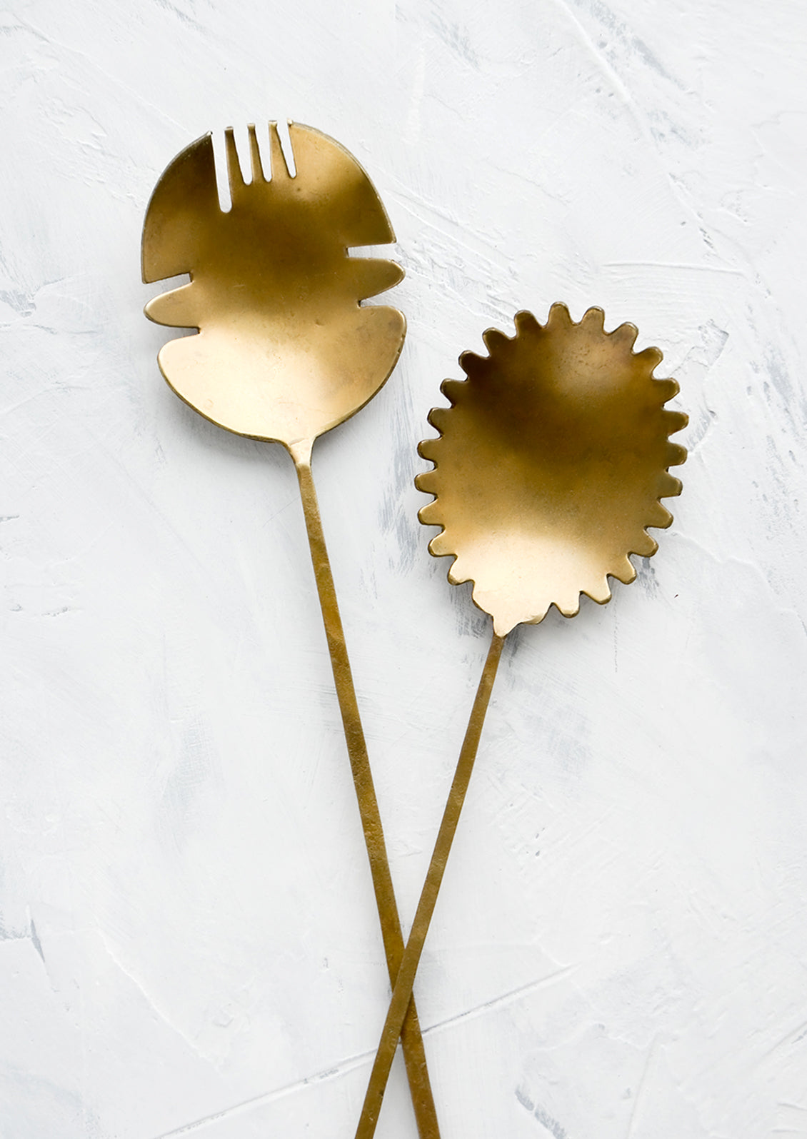 A pair of salad servers made from antiqued brass, shaped in a prehistoric-inspired design.