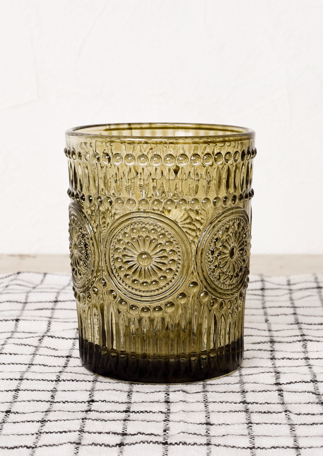 An olive green glass cup in embossed design.