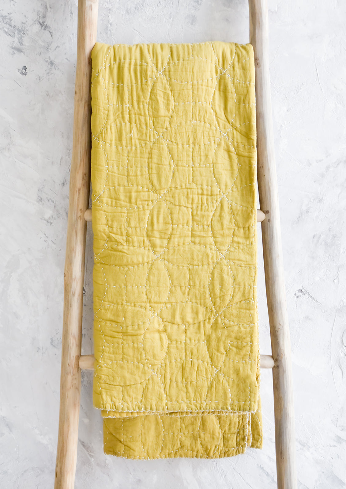 Chartreuse colored cotton throw with overlapping circle patterned embroidery, hanging on display ladder