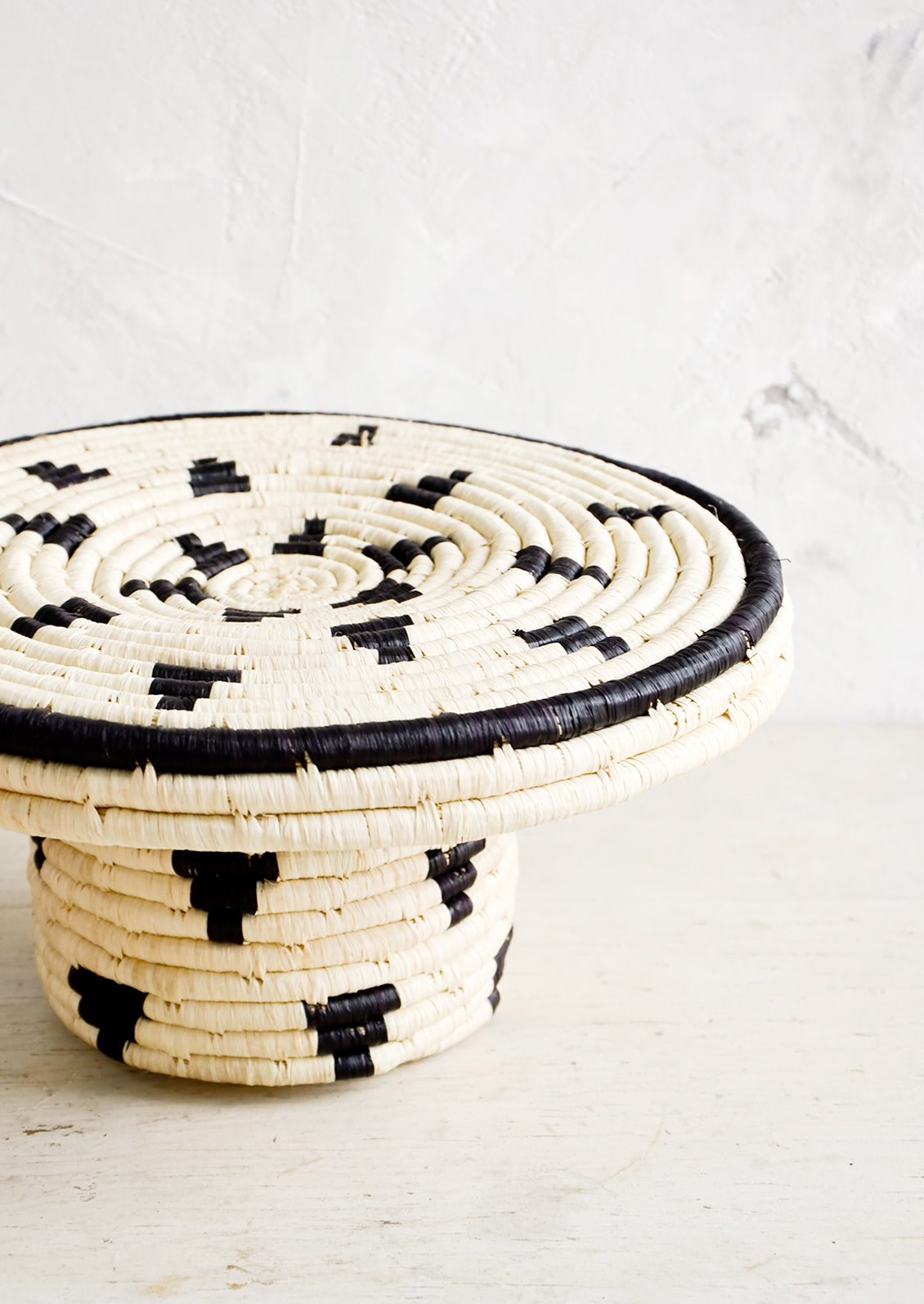 Round woven raffia cake stand in natural with black triangle print