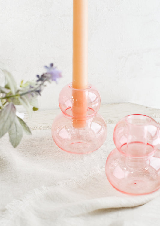 Bubble shaped glass taper candle holders in pink, on a table.