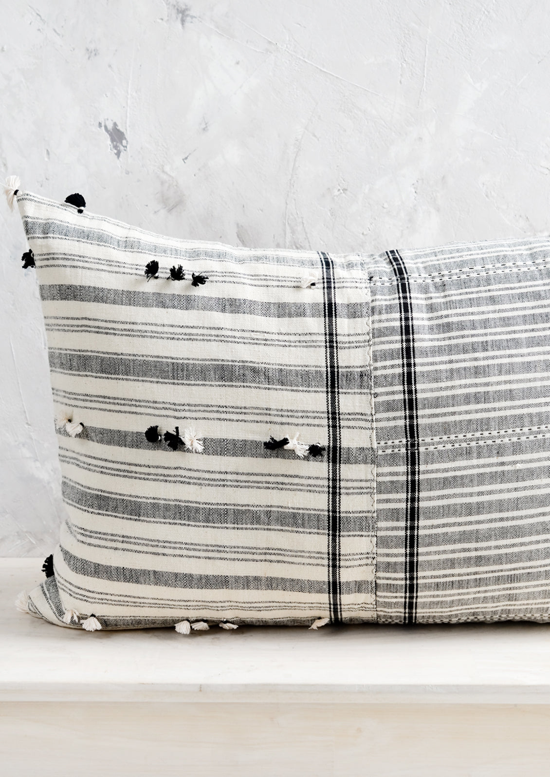 A lumbar throw pillow in black and white madras fabric with tassel detailing throughout.