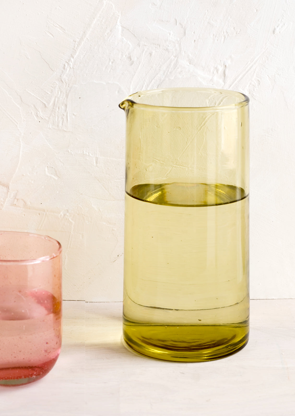 A glass pitcher in green glass with pink glass cup.