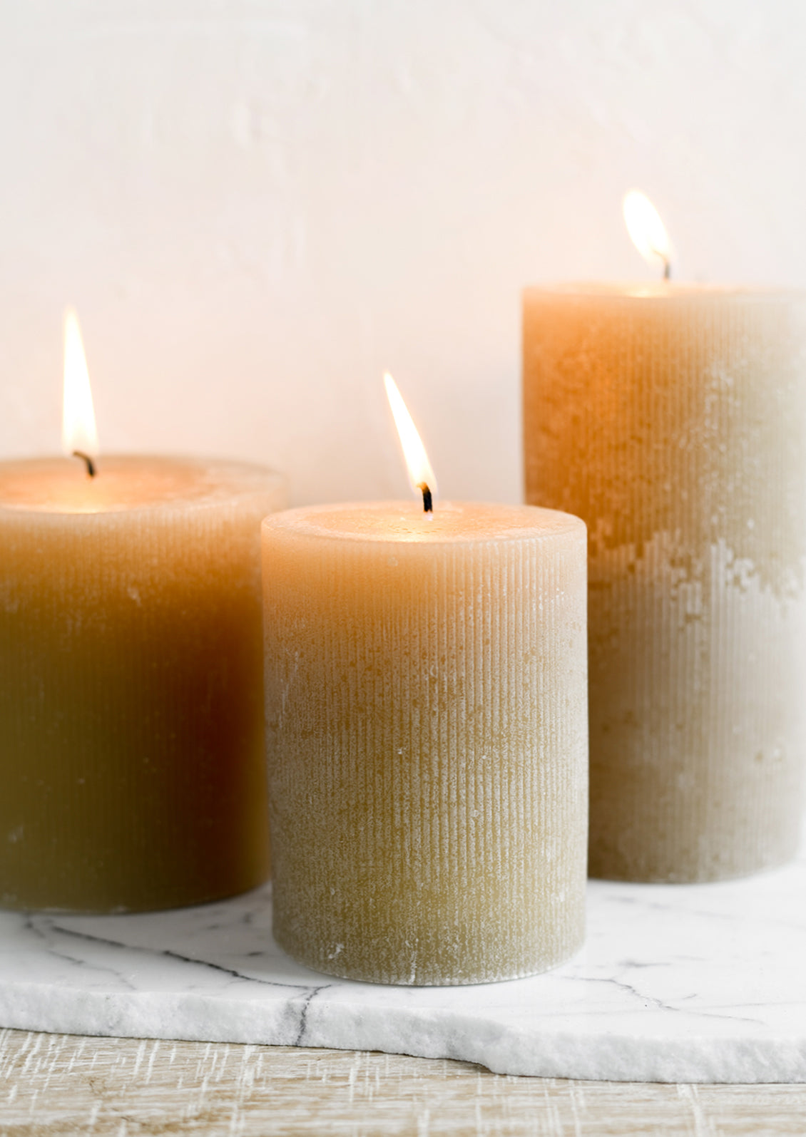 Three tan colored pillar candles in assorted sizes.