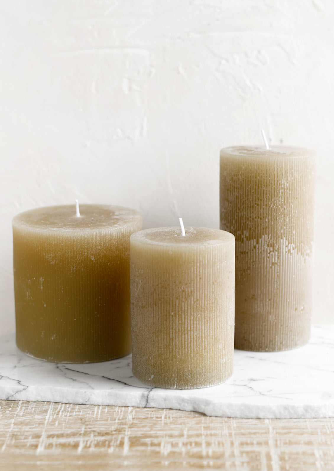 Three tan colored pillar candles in assorted sizes.