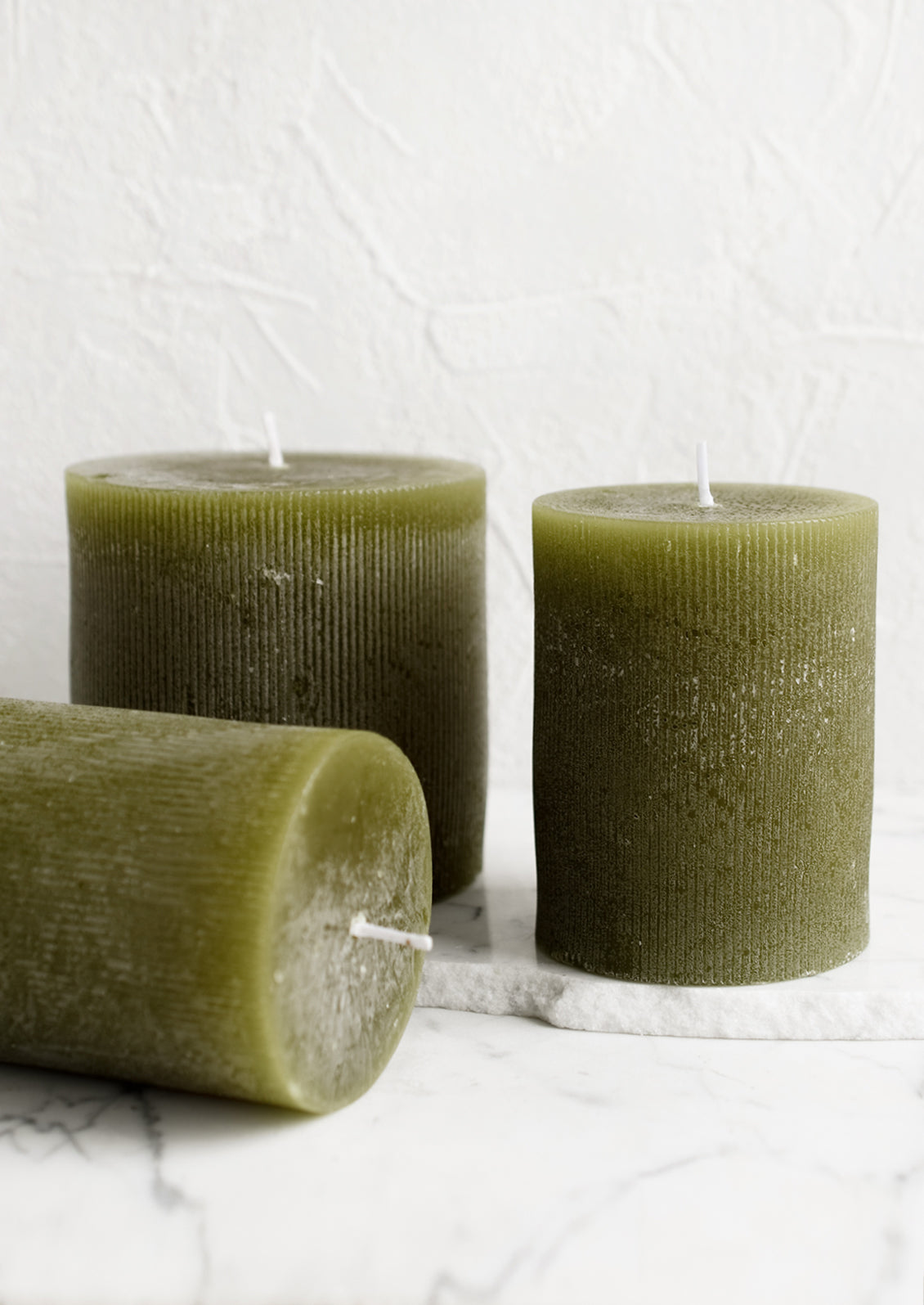 Three green colored pillar candles in assorted sizes.