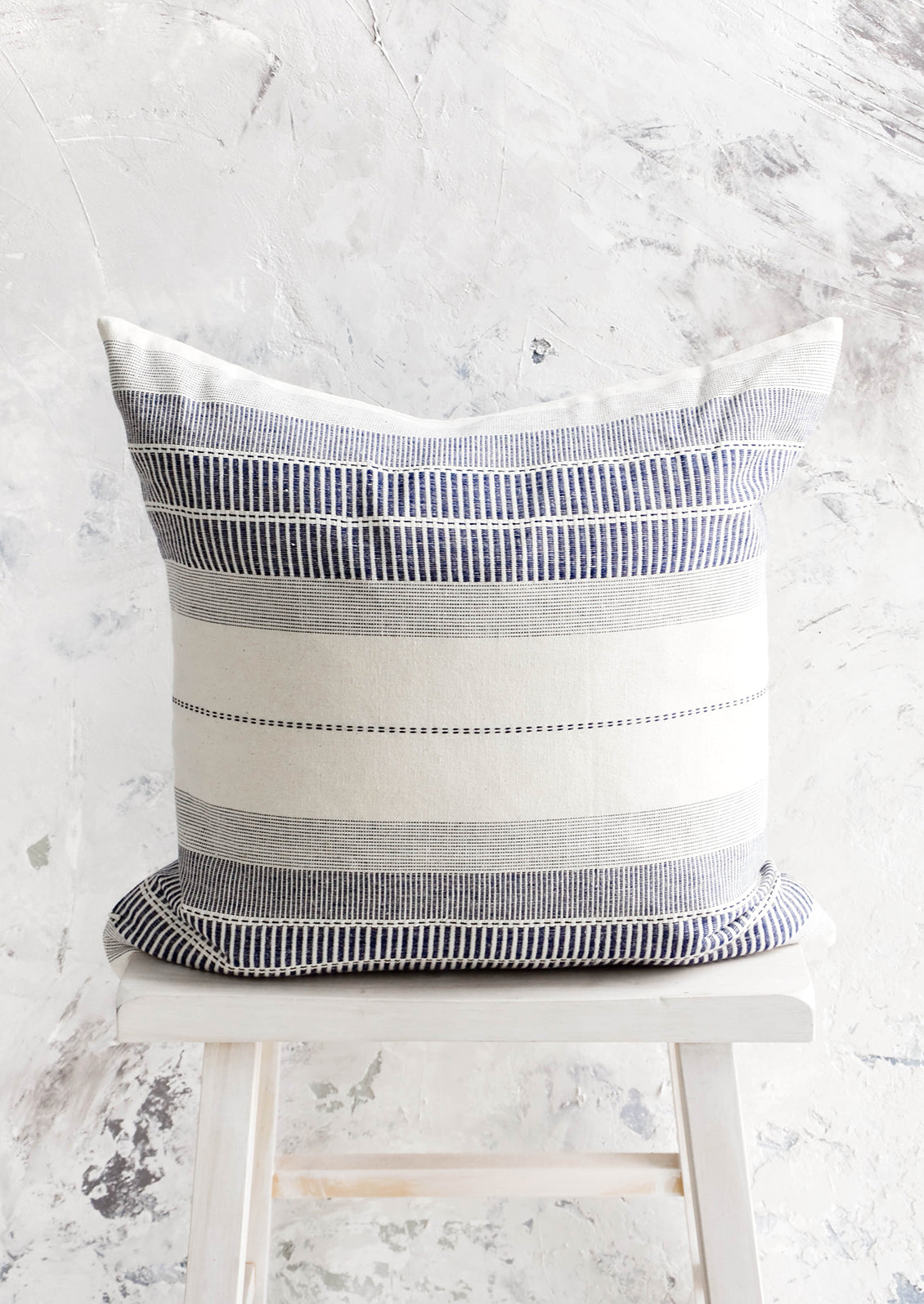 Square throw pillow in natural cotton with blue embroidery in striped patterns.