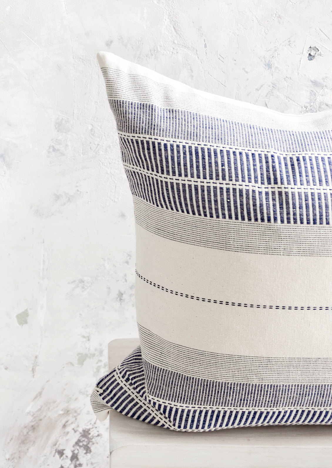 Square throw pillow in natural cotton with blue embroidery in striped patterns.