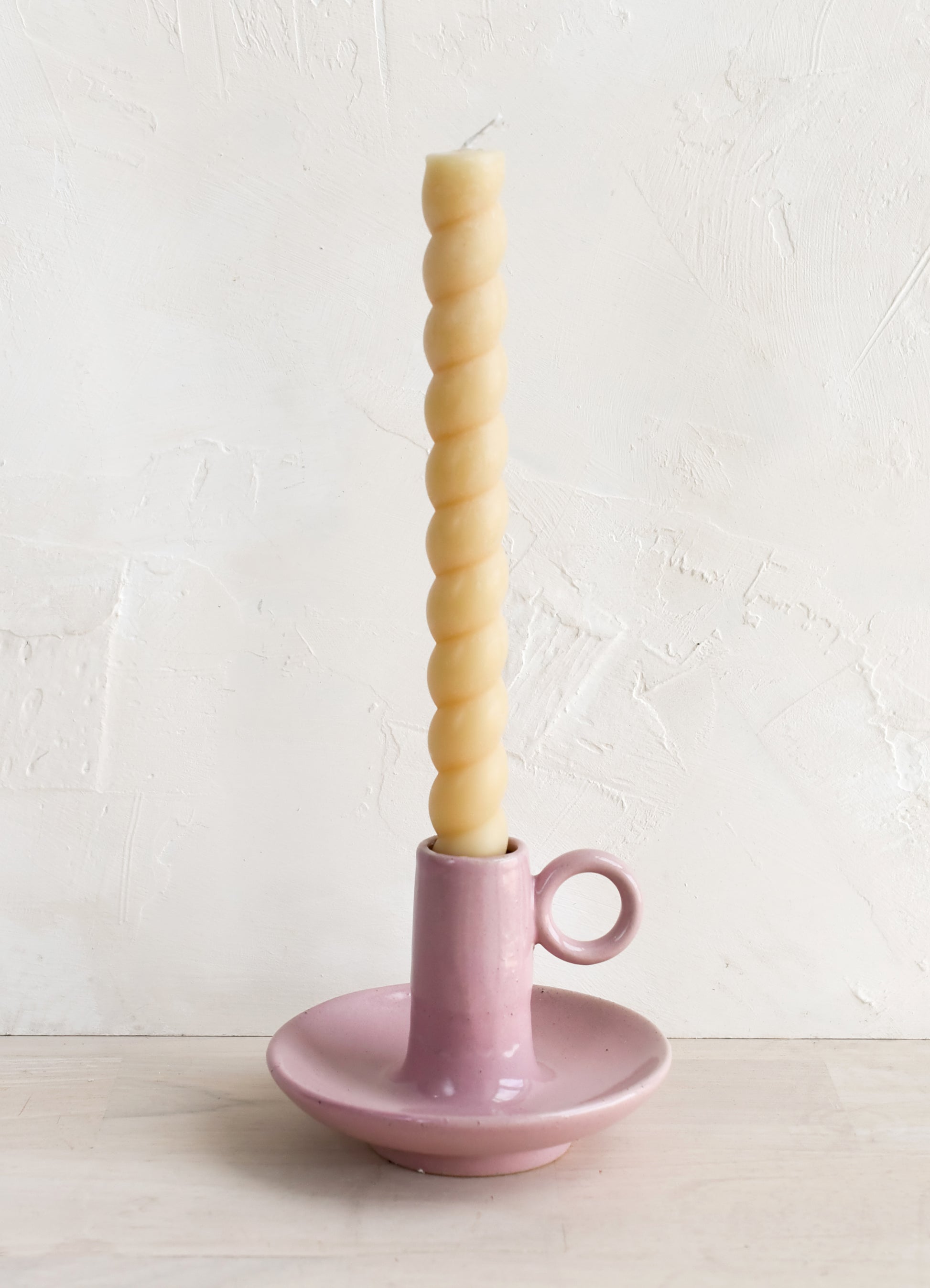 A pink taper holder holding a twisted taper candle.