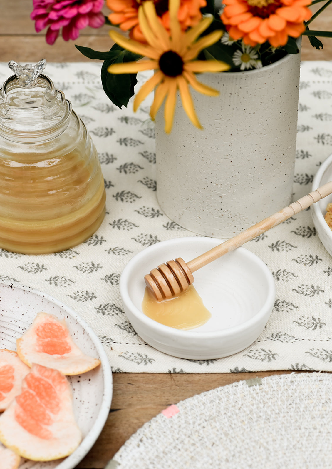 A table setting with honey jar and honey dipper in bowl.