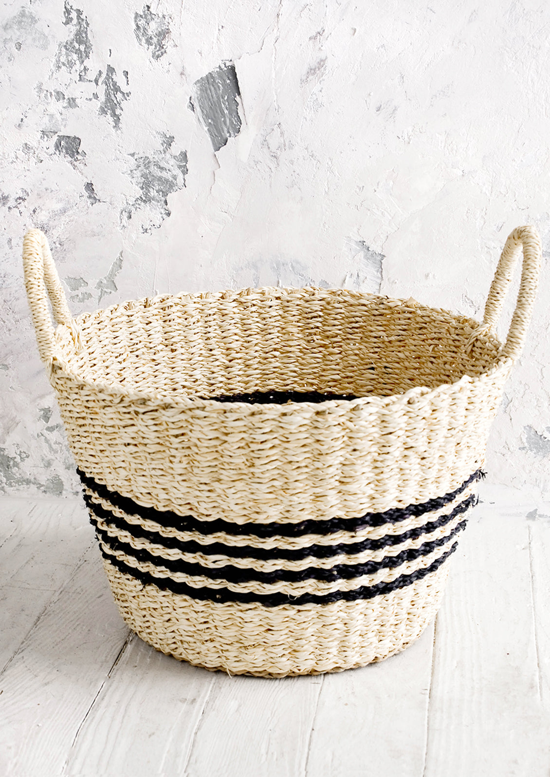 Round woven storage basket with thin black stripes, tapered bottom and two handles.