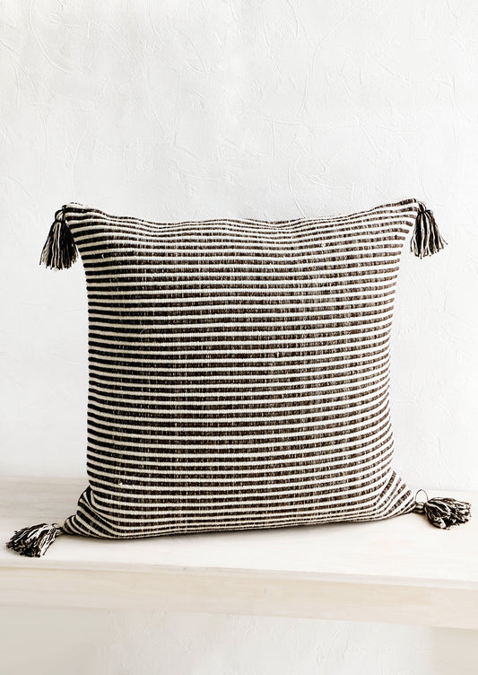 Large square throw pillow in textured dark brown and cream stripes, decorative tassel at each corner