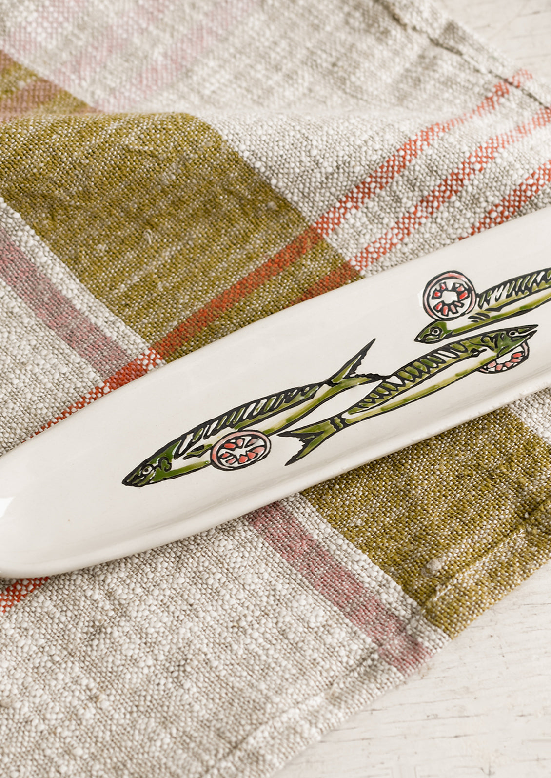 A long and skinny white ceramic dish with green sardine print.