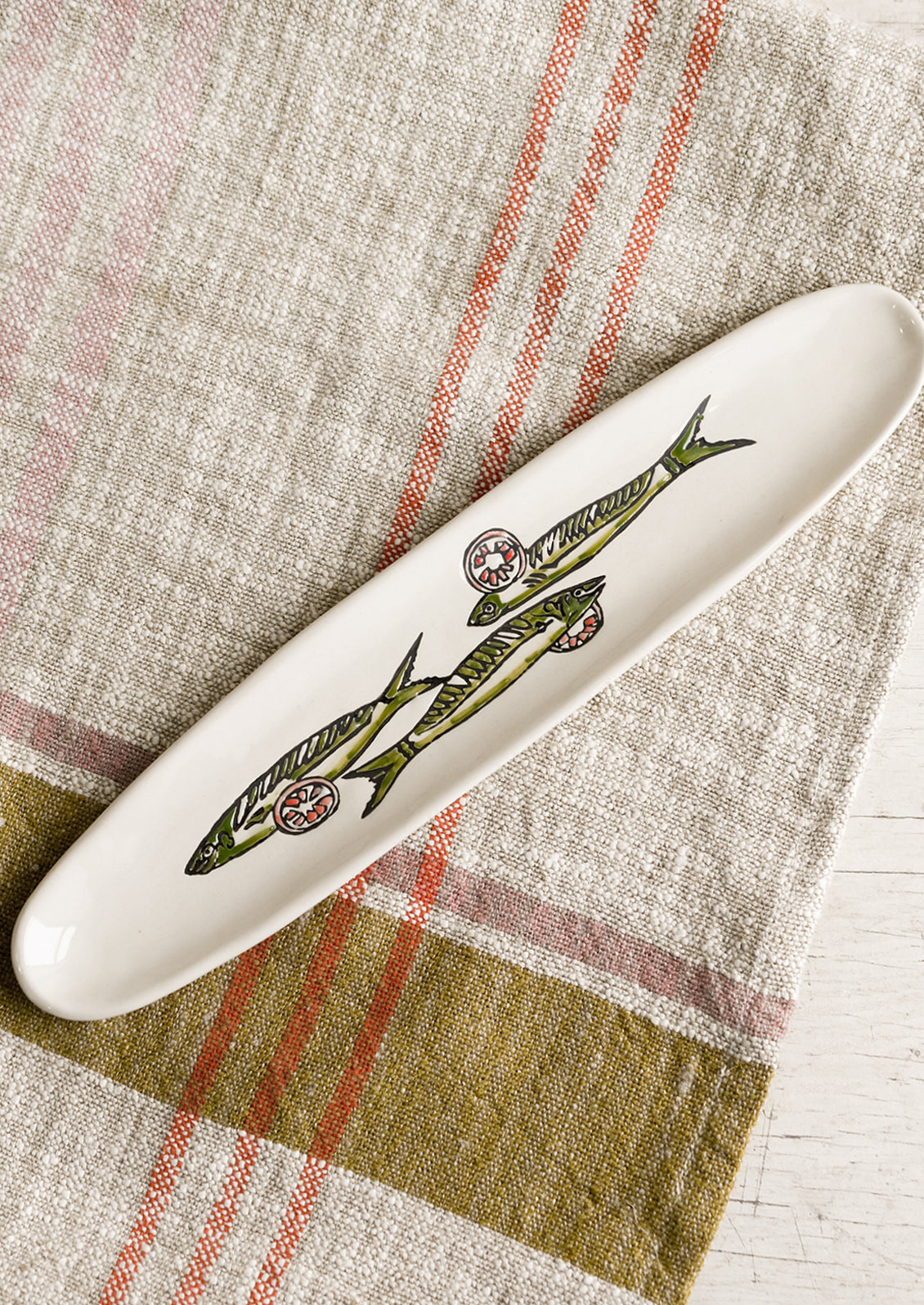 A long and skinny white ceramic dish with green sardine print.