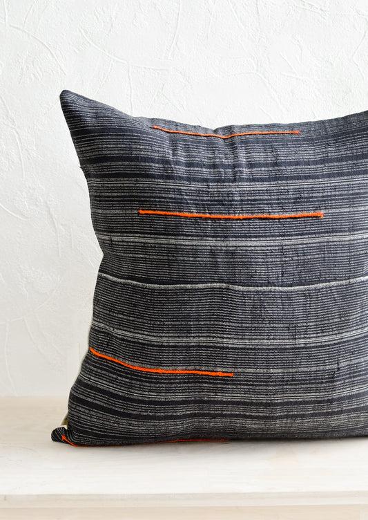 A square throw pillow made from dark blue fabric with grey stripes and embroidered orange lines.