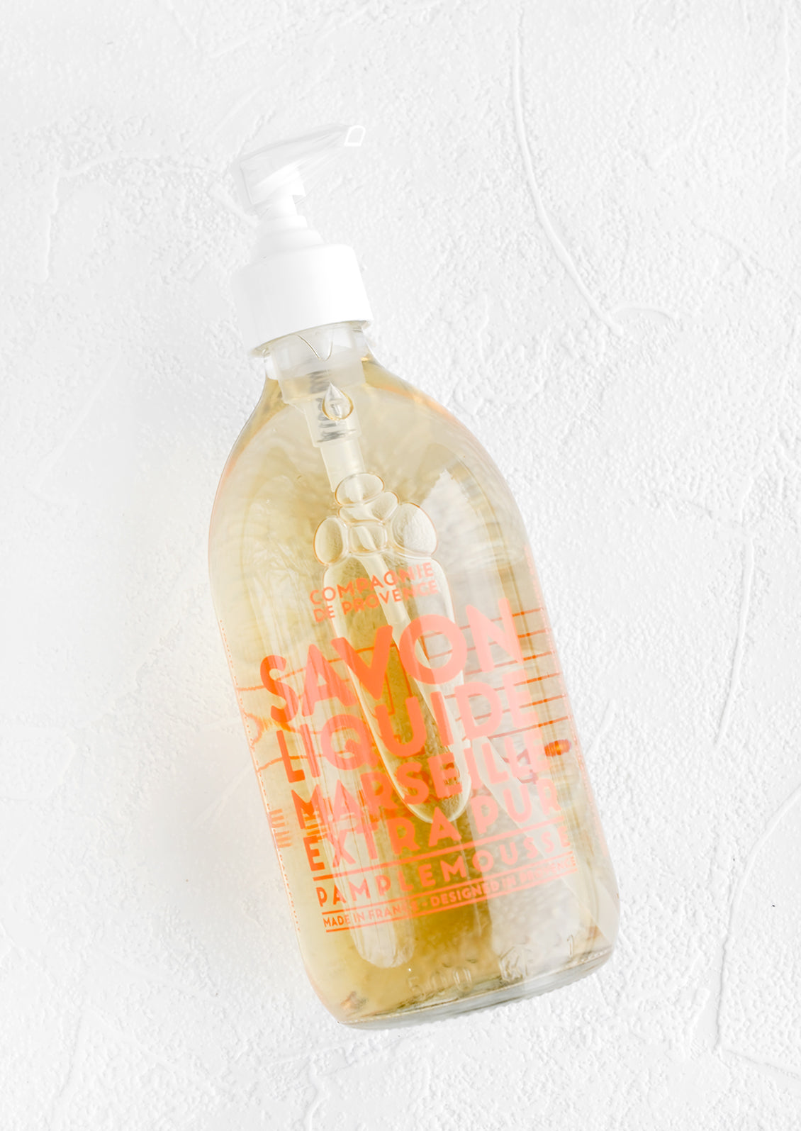 A clear glass soap bottle with bold orange text printed on bottle